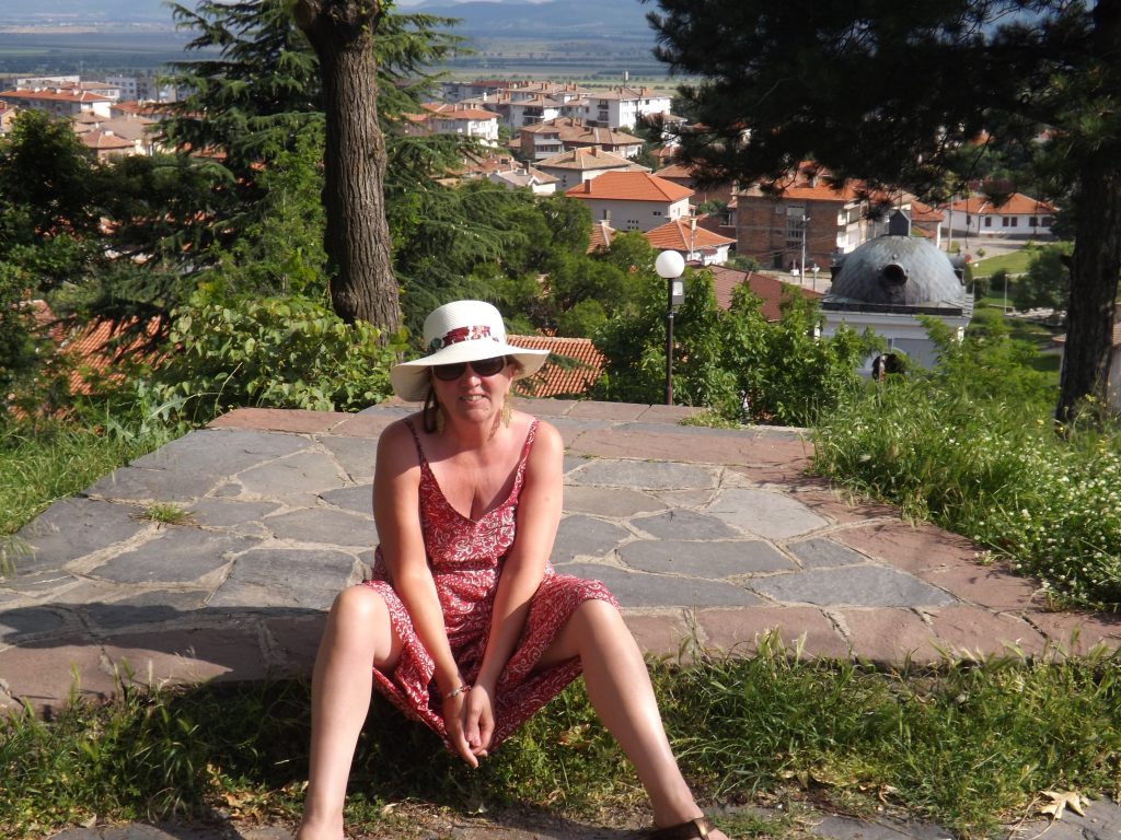 me on a very hot summer’s day Sitting with my back to the town of support in the foothills of the mountains wearing a red dress, sunglasses, and a sun hat